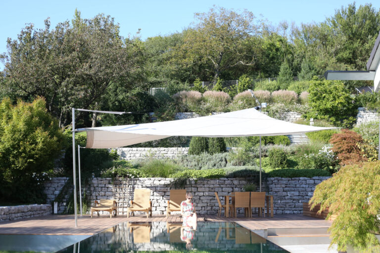 Ein klimafreundlicher Garten mit Pool, Sonnensegel und naturnaher Bepflanzung schafft angenehme Aufenthaltsbereiche und schützt vor sommerlicher Hitze.